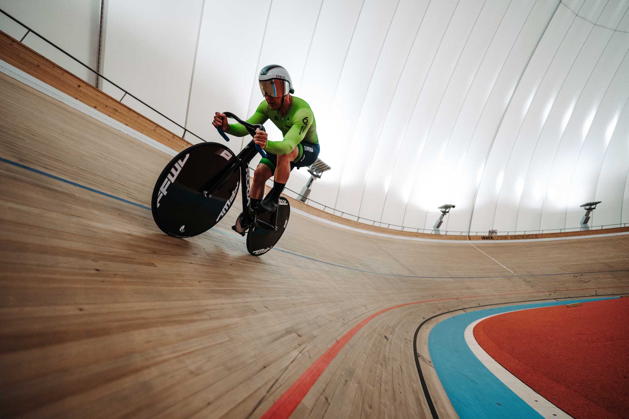 Velodromski kolesar v zelenem dresu med vožnjo po nagnjeni stezi v Novem mestu